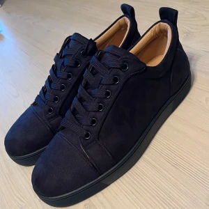 Mörkblåa sneakers från Christian Louboutin - Snygga svarta sneakers i mocka från Christian Louboutin med den ikoniska röda sulan. Skorna har snörning och en rund tå, vilket ger en stilren look. Pris kan såklart diskuteras. Om du har några frågor är de bara att fråga på!