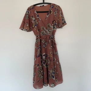 Blommig klänning från bubbleroom  - Säljer en vacker blommig klänning från bubbleroom. Klänningen har ett knytband i midjan för en smickrande passform. Den har en v-ringad hals och ett härligt blommönster i flera färger. Strl 36/38. 