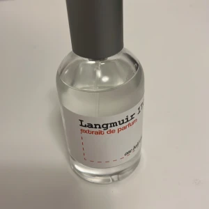 Langmuir 17 Extrait de Parfum - Elegant och sofistikerad flaska med Langmuir 17 Extrait de Parfum. Den genomskinliga glasflaskan har en stilren design med en grå kork och en vit etikett med röd och svart text. Perfekt för den som söker en unik doftupplevelse. Den är inspirerad av Lv imagination