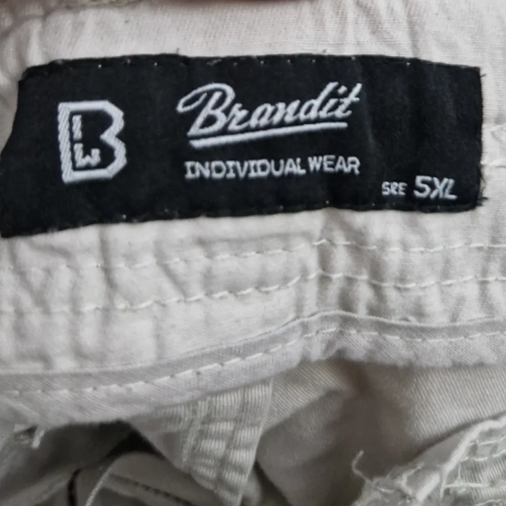 Säljer ett par beige cargopants från Brandit med flera praktiska fickor och en avslappnad passform. Perfekta för en baggy fit. Köptes för 600 kr.. Farkut & Housut.