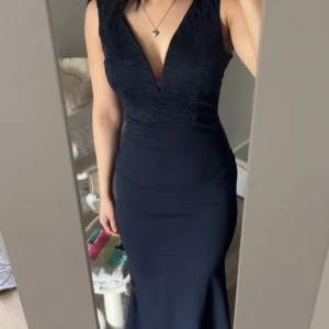 Marinblå långklänning från Wal G - Elegant marinblå långklänning med spetsdetaljer och djup v-ringning. Klänningen har en figurnära passform och är perfekt för speciella tillfällen. Den är ärmlös och har en stilren design som framhäver silhuetten.