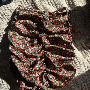 Blommig kortkjol - Säljer en söt blommig kortkjol med ett färgglatt mönster i rött, rosa och grönt. Kjolen har en tight passform och är elastisk. Hör av dig vid frågor eller för prisförslag!