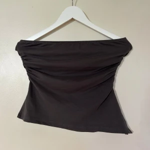 Mörkgrå tubtopp - Säljer en stilren mörkgrå tubtopp med rynkade detaljer på sidorna. Perfekt för en enkel och chic look. Passar bra till både jeans och kjol.