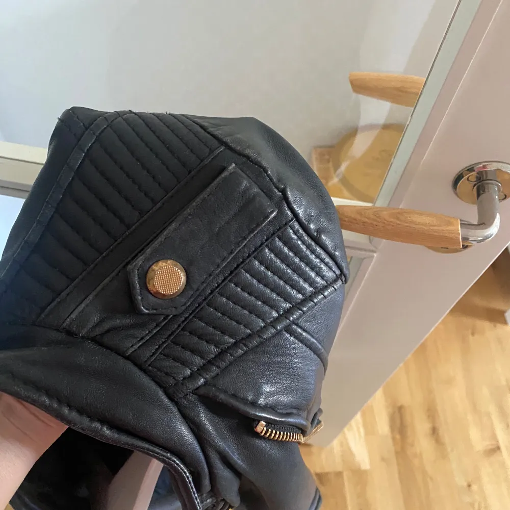 Snygg svart skinnjacka från Zara Basic med coola detaljer som dragkedjor och knappar i guld. Jackan har en modern design med långa ärmar och quiltade axelpartier. Perfekt för en stilren look! Äkta skinn, ny pris 3900kr. Takit.