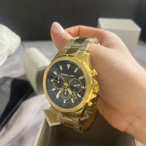 Guldfärgad klocka från Michael Kors hellt ny. Pris 3200kr säljer billigt  - Snygg guldfärgad klocka från Michael Kors med svart urtavla och flera små urtavlor. Perfekt accessoar för att lyfta din stil. Kommer i originalförpackning.