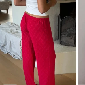 Röda broderade byxor från Nelly - Säljer ett par snygga röda byxor från Nelly med broderade detaljer. Byxorna har en avslappnad passform och är perfekta för en chill dag hemma. De har en elastisk midja med snörning för extra komfort. Aldrig använda men råkade dra bort lappen, men på tredje bilden ser man lappen❤️