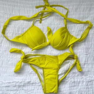 Gul bikini med knytband - Snygg gul bikini med knytband i både över- och underdel. Toppen har vadderade kupor och knytning i nacken och ryggen. Perfekt för soliga dagar på stranden eller vid poolen. Storlek S.