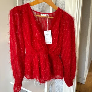Röd glittrig blus från Vila - Säljer en röd glittrig blus från Vila med långärmad design och v-ringning. Blusen har en luftig och festlig look med glittrande detaljer som ger extra glamour. Perfekt för speciella tillfällen!