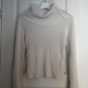 Beige ribbad tröja från KappAhl - Säljer en krämvit ribbad tröja från KappAhl med en unik krage och knappar på både krage och ärmar. Storlek 34-36