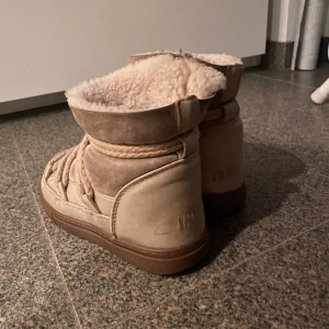 Beige boots med pälsfoder - Säljer ett par mysiga beige boots med pälsfoder och snörning. Perfekta för kalla dagar med sin varma insida och robusta sula. De har en rund tå och är gjorda i mocka och syntetmaterial.