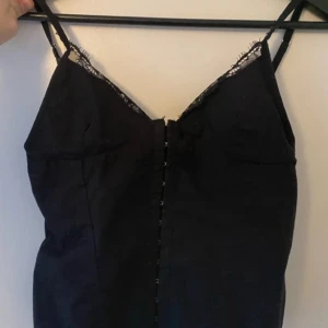 Svart korsettopp från Zara - Snygg svart korsettopp från Zara med spetsdetaljer och smala axelband. Toppen har en knäppning framtill. Den är i fint skick förutom några metall krokar som man knäpper med som är lite tillböjda men det är lätt att böja till dom om man stör sig på det.
