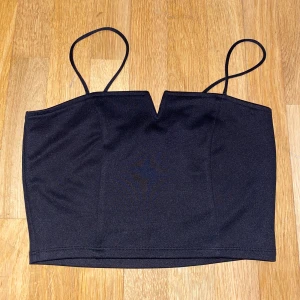 Svart tubtopp från Bik Bok - Snygg svart tubtopp från Bik Bok med smala axelband och en stilren design. Perfekt för en trendig look. Toppen har en liten v-formad detalj framtill som ger en extra touch.