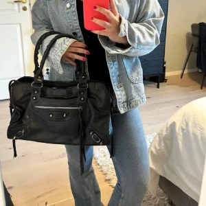 Svart skinn handväska - Snygg svart skinn handväska med dragkedja och dekorativa detaljer. Perfekt för att bära dina dagliga nödvändigheter med stil. Den har robusta handtag och en praktisk storlek för enkel användning. Perfekt skolväska där datorn på plats och mycket annat! Pris kan diskuteras 