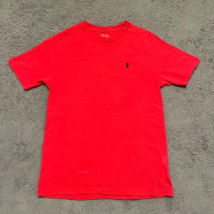 Röd t-shirt från Ralph Lauren - Snygg röd t-shirt från Ralph Lauren med klassisk broderad logga på bröstet. Perfekt för en avslappnad stil. Tillverkad i mjukt material för extra komfort.