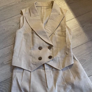 Beige kostymväst och byxor - Skräddare sydd beige kostymväst med dubbelknäppning och matchande byxor. Passar för någon 1m60 och 49kg. Oanvänd 