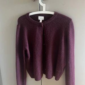 Vinröd kofta från H&M - Säljer en mysig vinröd kofta från H&M. Den har långa ärmar och knäppning framtill. Perfekt för kyliga dagar och enkel att matcha med olika outfits.