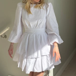 Vit klänning med volanger - Säljer en söt vit klänning med volanger och öppen rygg. Klänningen har långa ärmar och knytning i ryggen. Perfekt till studenten. Klänningen är helt ny och har lapparna kvar från Nalina. Passar mig som vanligtvis har xs och är 158. (Passar även nån gin lite längre) Nypris 1700kr jag säljer den för 1500kr. Tveka inte att höra av dig om du har någon fråga! 🥂💖