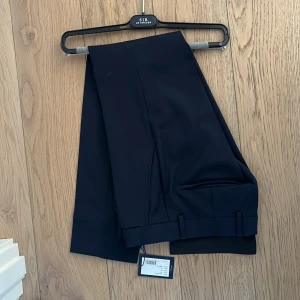 Svarta kostymbyxor från sir Sweden  - Eleganta svarta kostymbyxor från Sir Sweden . Byxorna har en klassisk design med knapp och dragkedja i midjan. Perfekta för en stilren look. Storlek 42 