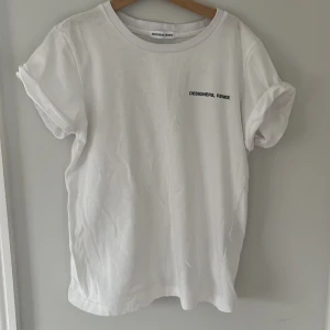 Vit t-shirt från Designers Remix - Säljer en stilren vit t-shirt från Designers Remix med svart text på bröstet. T-shirten har en klassisk rund hals och korta ärmar. Frakt ingår inte i priset!