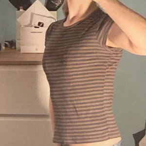 Randig kortärmad topp - Säljer en randig topp i brunt och grått med korta ärmar. Toppen har en tight passform och är perfekt för en avslappnad stil. Den är gjord i ett mjukt och bekvämt material.