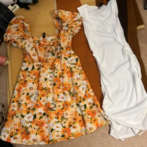 Orange blommig klänning med puffärmar och vitt klänning  - Säljer en färgglad orange klänning med blommigt mönster och puffiga kortärmar. Klänningen har en söt snörning framtill och en luftig passform, perfekt för varma dagar. 🌼 vita har snören som man kan fixa kort storleken som man vill 