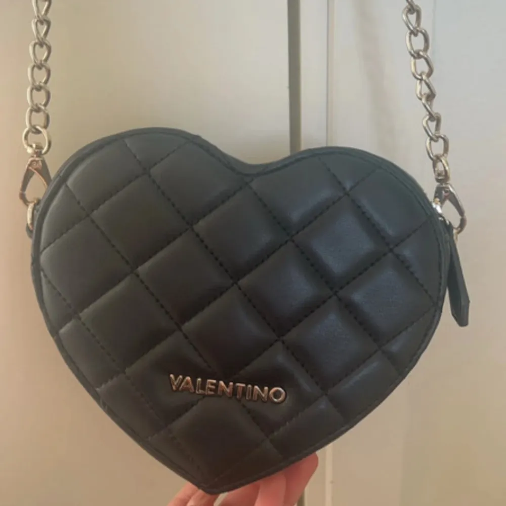 Snygg svart hjärtformad axelväska från Valentino med quiltad design och kedjerem. Väskan har en dragkedja upptill och är perfekt för att bära dina nödvändigheter med stil. Den eleganta designen gör den till ett utmärkt val för speciella tillfällen.Den är i perfekt skick utvändigt och ser ut som ny! Endast lite smuts inuti, men inget som påverkar användningen. Öppen för förhandling.. Laukut & Käsilaukut.