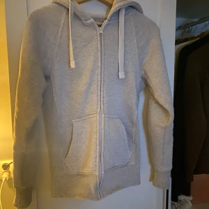 Grå mjukisbyxor och hoodie - Säljer ett russemerch set med grå mjukisbyxor och matchande hoodie. Hoodien har dragkedja och snörning i huvan, medan byxorna har snörning i midjan. 