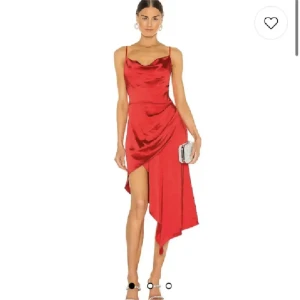 Röd satin klänning - Snygg röd klänning i satin med asymmetrisk design och smala axelband. Klänningen har en elegant drapering och en slits framtill som ger en stilfull look. Perfekt för festliga tillfällen.
