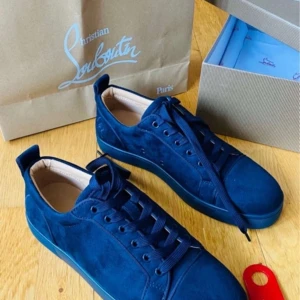 Marinblåa sneakers från Christian Louboutin - Snygga marinblåa sneakers från Christian Louboutin med den ikoniska röda sulan. Skorna har snörning och är tillverkade i ett elegant material som ger en lyxig känsla. Perfekta för att ge din outfit en exklusiv touch.