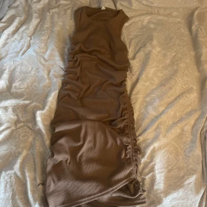 Brun ärmlös klänning - Snygg brun ärmlös klänning med rynkade detaljer på sidorna. Perfekt för en stilren look. Klänningen har en tight passform och är gjord i ett mjukt material. Mycket stretchig.
