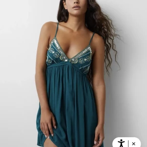 Turkos klänning med broderade detaljer - Snygg turkos klänning som passar bra till sommaren. Med jättefina broderade detaljer i guld och silver. Säljer då den är för liten i bysten på mig och har därför inte använt den mycket.💕