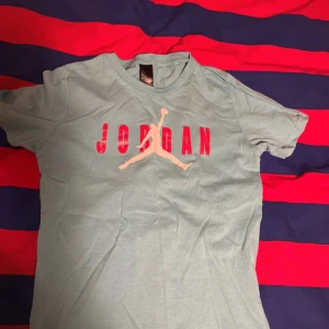 Ljusblå Jordan t-shirt - Säljer en ljusblå Jordan t-shirt med det ikoniska logotyptrycket i rött och vitt på framsidan. T-shirten är kortärmad och tillverkad i bomull, vilket gör den bekväm och perfekt för vardagsbruk.