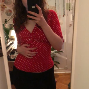 Röd prickig topp från Passage - Säljer en röd topp med vita prickar från Passage. Toppen har en v-ringad design med trekvartsärmar. Perfekt för en färgglad look!