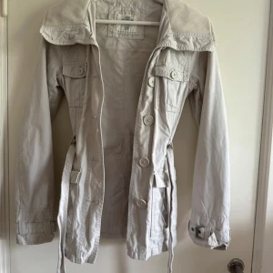 Vår kappa med skärp - Snygg jacka från H&M med knappar, flera fickor & fina detaljer. Jackan har långa ärmar och en krage med knappar. Perfekt för vår och höst. Nyskick🌸