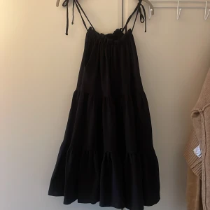 Klänning med knytband  - Svart klänning med lite volanger från Hm. Man kan knyta banden själv samt dra åt halsringningen och få en mer halterneck stil! Säljes då den är lite för stor för mig