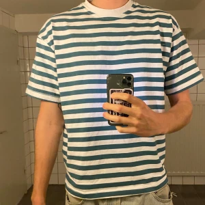 Randig t-shirt från H&M - Säljer en vit och blå randig t-shirt från H&M. T-shirten har klassisk passform med rund halsringning och korta ärmar. Perfekt för en avslappnad stil och enkel att matcha med jeans eller shorts.