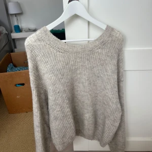 Grå stickad tröja från American Vintage - Mysig och fluffig grå stickad tröja från American Vintage. Tröjan har en rund halsringning och långa ärmar, perfekt för lager-på-lager under kyliga dagar. Enkel och stilren design som passar till det mesta.