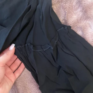 Svart blus från Indiska - Säljer en svart blus från Indiska med knytband vid halsen. Blusen har en lös passform och är perfekt för en avslappnad stil. Den är tillverkad i ett lätt och luftigt material.