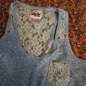 Blå linnetopp från Superdry - Säljer en snygg blå linnetopp från Superdry med spetsdetaljer på ryggen och en liten spetsficka fram. Perfekt för varma dagar och ger en stilren look. 🩵