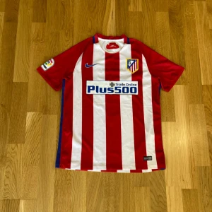 Atlético Madrid 2016-2017 matchtröja Griezmann  - Säljer en Atlético Madrid fotbollströja från Nike med Griezmann 7 på ryggen. Tröjan är i fint skick utöver att trycket har släppt lite (se bild 2). Tröjan är äkta! Storlek Small 