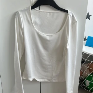 Vit långärmad topp med rund hals - En enkel och stilren vit långärmad topp med rundad, djup urringning. Perfekt att matcha med jeans eller kjol för en clean look. Mjuk och skön bomullskänsla.