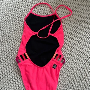 Rosa baddräkt från Jolyn med färgglada band - Säljer en snygg rosa baddräkt från Jolyn. Modellen heter Julian. Storlek 28. Acceptabelt skick. Lite sliten på rumpan, men i övrigt bra skick.  