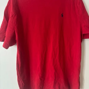 Röd t-shirt från Polo Ralph Lauren - Säljer en klassisk röd t-shirt från Polo Ralph Lauren med liten broderad logga på bröstet. T-shirten har normal passform och är tillverkad i mjuk bomull. Perfekt för en stilren och enkel look.