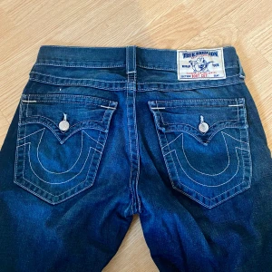 True Religion Bootcut Jeans - Mörkblå jeans från true religion, lågmidjade!! Verkligen såååå snygga! Bootcut/baggy modell. Skulle uppskatta storleken till M, men det står 32. Så coola! 🙏🏼Liten slitning där nere, se sista bilden. Inget man tänker på! 