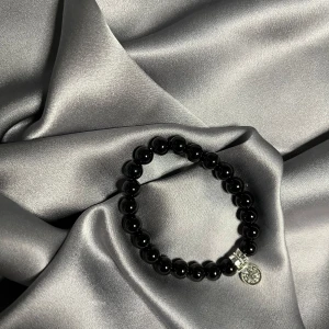 Två pärlarmband med berlocker - Säljer två elastiska armband med runda pärlor, ett i svart och ett i rött. Båda har små silverfärgade detaljer och en berlock. Perfekt accessoar för att lyfta din outfit.