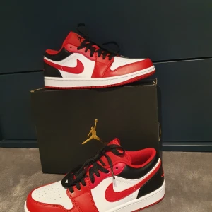Nike Air Jordans 1 low - Snygga Nike Air Jordans i en klassisk färgkombination av rött, vitt och svart. Skorna har en rund tå och snörning framtill. Perfekta för dig som vill ha en stilren och sportig look.