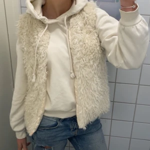 Vit pälsväst - Säljer en fluffig och mysig vit pälsväst perfekt för lager-på-lager stil. Västen är ärmlös och har en öppen design som gör den lätt att matcha med olika outfits. Perfekt för kyligare dagar när du vill hålla dig varm och trendig.
