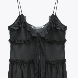 Svart volangprydd linnetopp från Zara - Supersöt svart linnetopp från Zara med tunna axelband och volangdetaljer. Toppen har knyt framtill och är dekorerad med små volanger längs kanterna och sömmarna. Perfekt att styla med jeans eller kjol. Den är i strl L men den är jätteliten i storleken så skulle säga att den sitter mer som S.