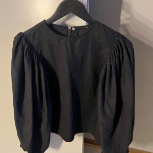 Svart blus med puffärmar - Säljer en svart blus med rund halsringning och långa, voluminösa puffärmar. Blusen har en rak passform och är tillverkad i ett lätt tyg som ger en elegant känsla. Perfekt för dig som gillar stilrena plagg med det lilla extra.