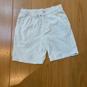 Vita frottéshorts från Kappahl - Säljer ett par vita shorts från Kappahl i mjuk frotté med resår och snörning i midjan. Perfekta för varma dagar eller att chilla i hemma. Klassisk passform och två sidofickor.